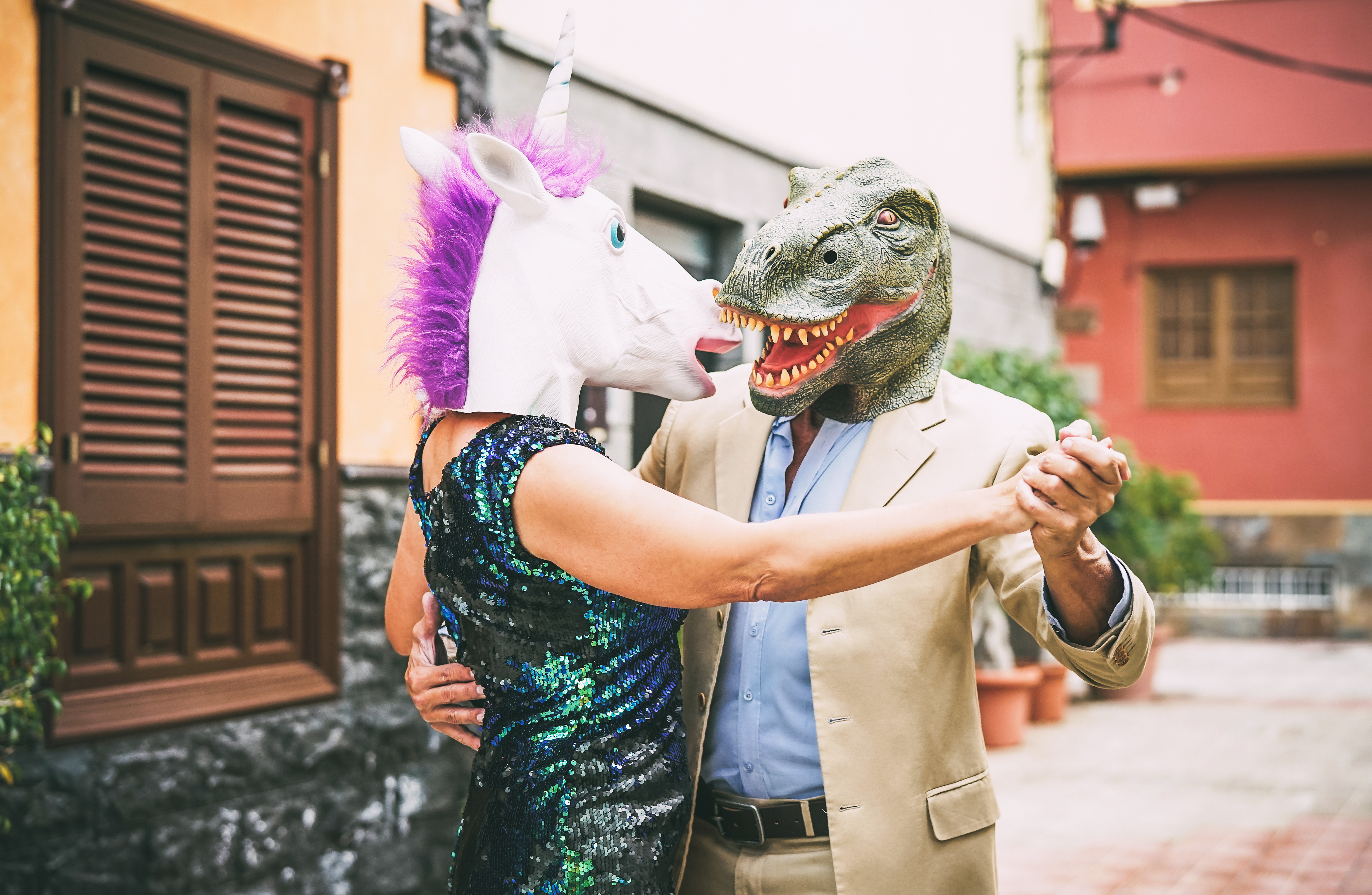 stock image of a couple dancing while wearing a dinosaur and a unicorn mask